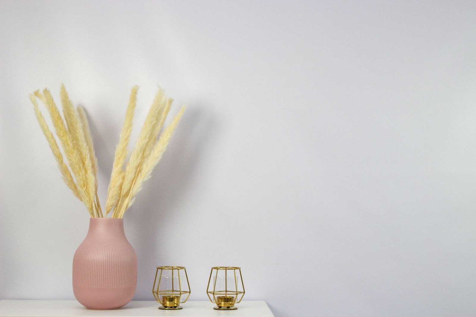 A soft blush vase with pale dried grass on a light grey surface